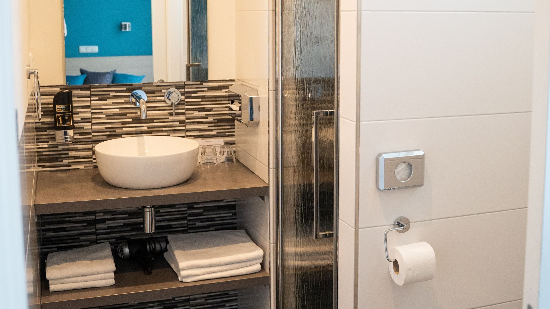 A bathroom with a white sink, a mirror, a towel rack, and a toilet paper holder.