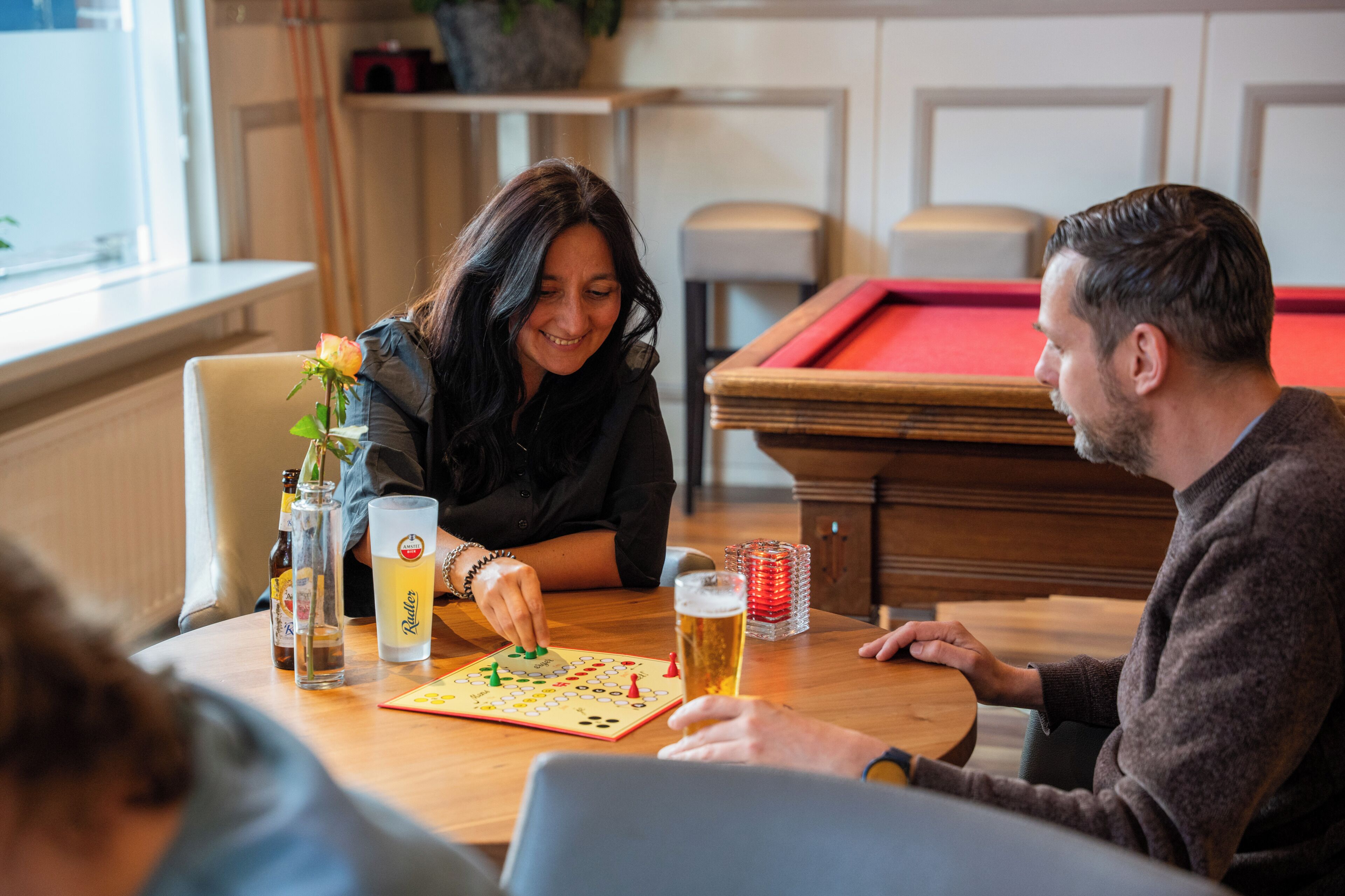 Un grupo de personas jugando un juego de mesa en una mesa de madera, con una mesa de billar al fondo.