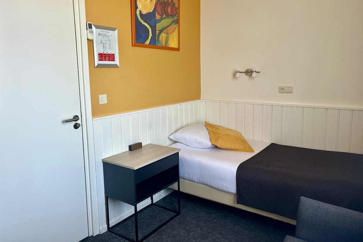 Een kamer met een bed, een tafeltje, een wandlamp en een schilderij.