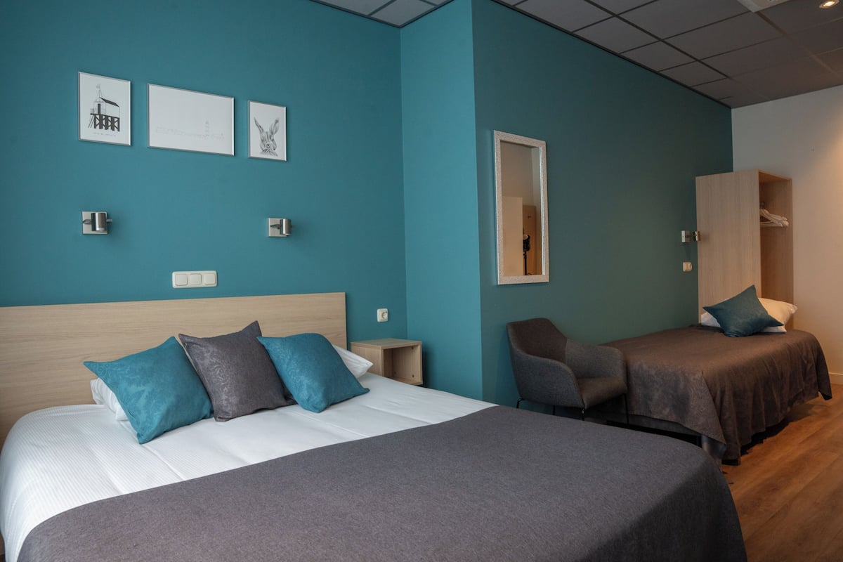 Een hotelkamer met een groot bed, een kleiner bed, een stoel, een garderobe en kunst aan de muur.
