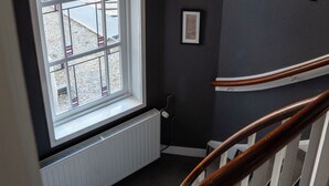 Una escalera con barandilla de madera, un radiador blanco y una ventana con vista al exterior.