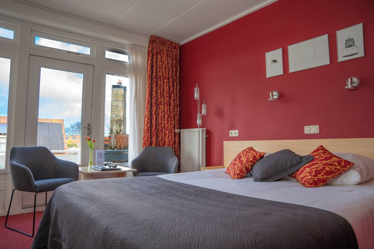 Een hotelkamer met een groot bed, twee stoelen, een bureau en uitzicht op een gebouw.