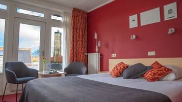 A hotel room with a large bed, two chairs, a desk, and a view of a building outside.