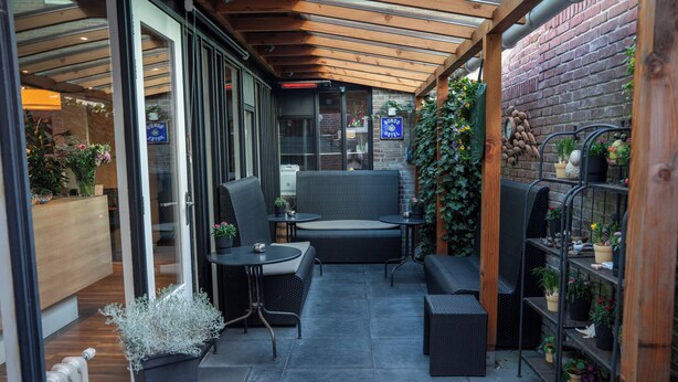 Un área de estar al aire libre techada con muebles de mimbre, una pared de ladrillo y plantas en macetas.