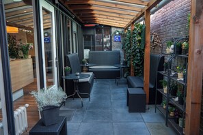 A covered outdoor seating area with wicker furniture, a brick wall, and potted plants. - Hotel Oepkes (West-Terschelling)