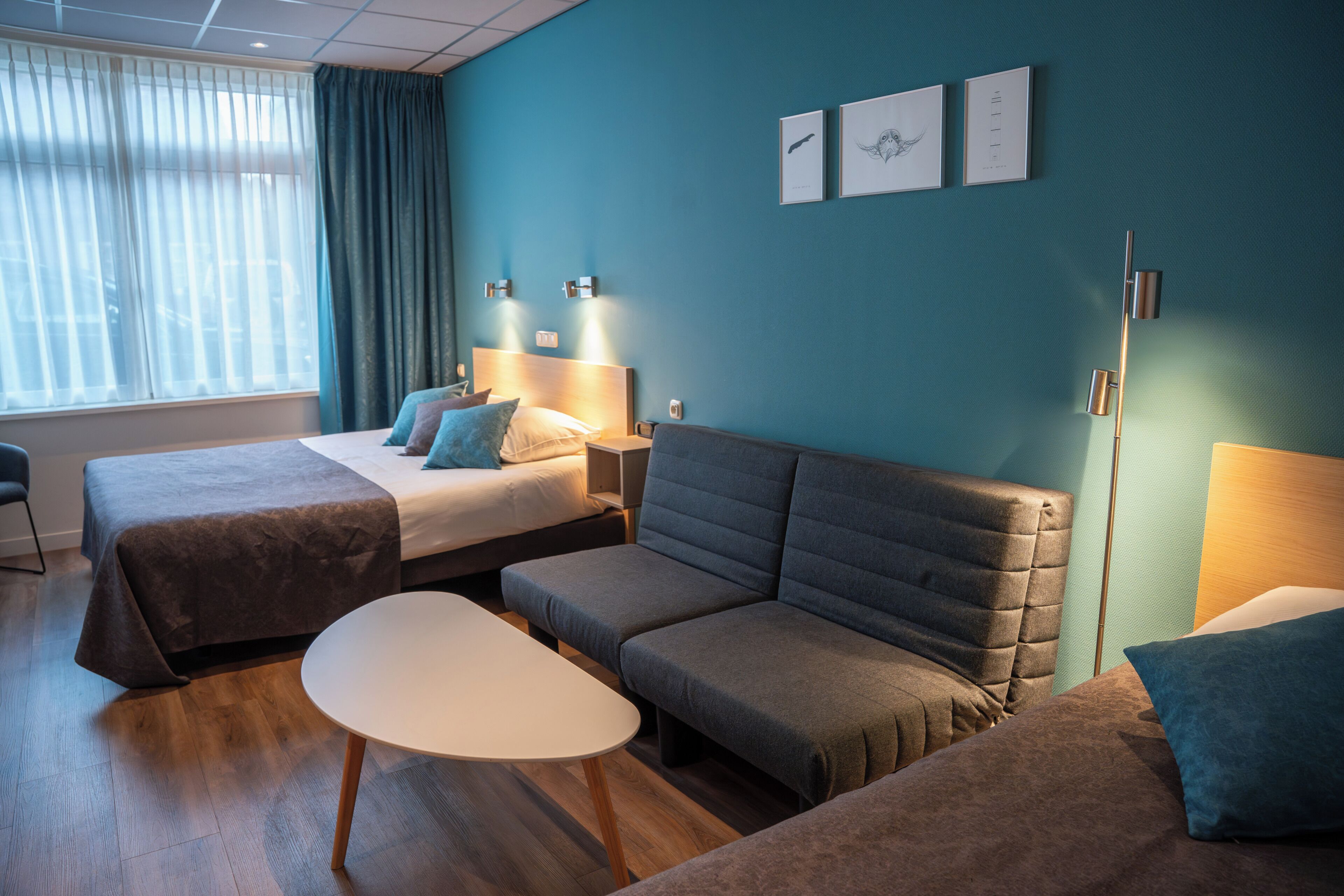 Ett hotellrum med två sängar, en soffa, ett bord och konstverk på väggen.