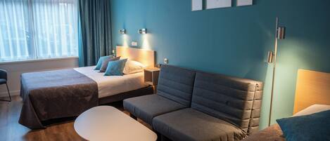 A hotel room with two beds, a sofa, a table, and artwork on the wall.