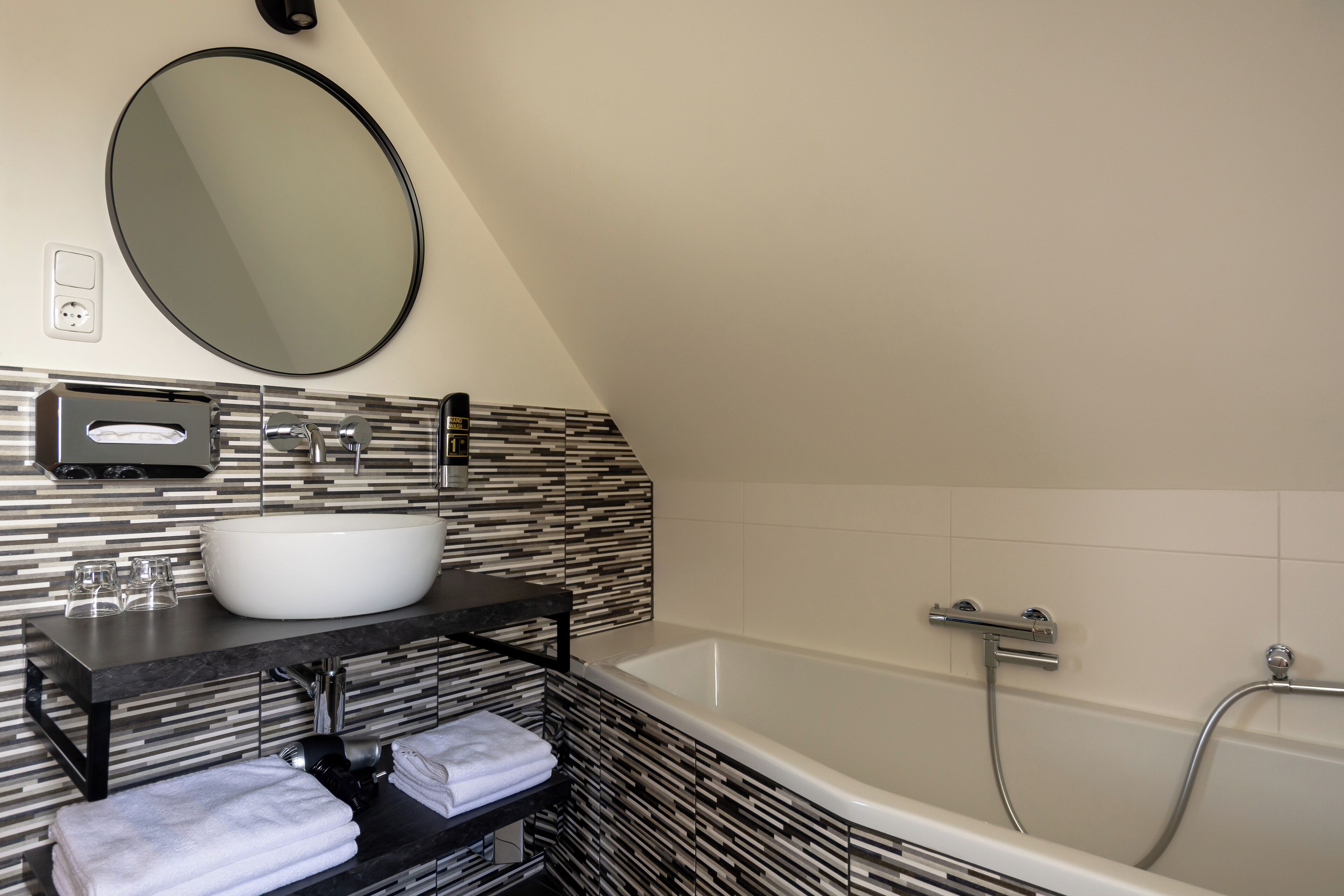 A modern bathroom with a large bathtub, a round mirror, a sink, and a towel rack.