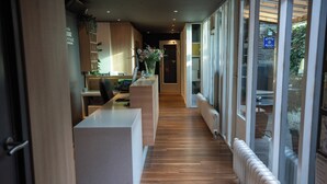 Un pasillo moderno de hotel con mostrador de recepción, suelo de madera y grandes ventanales que ofrecen vistas al exterior.