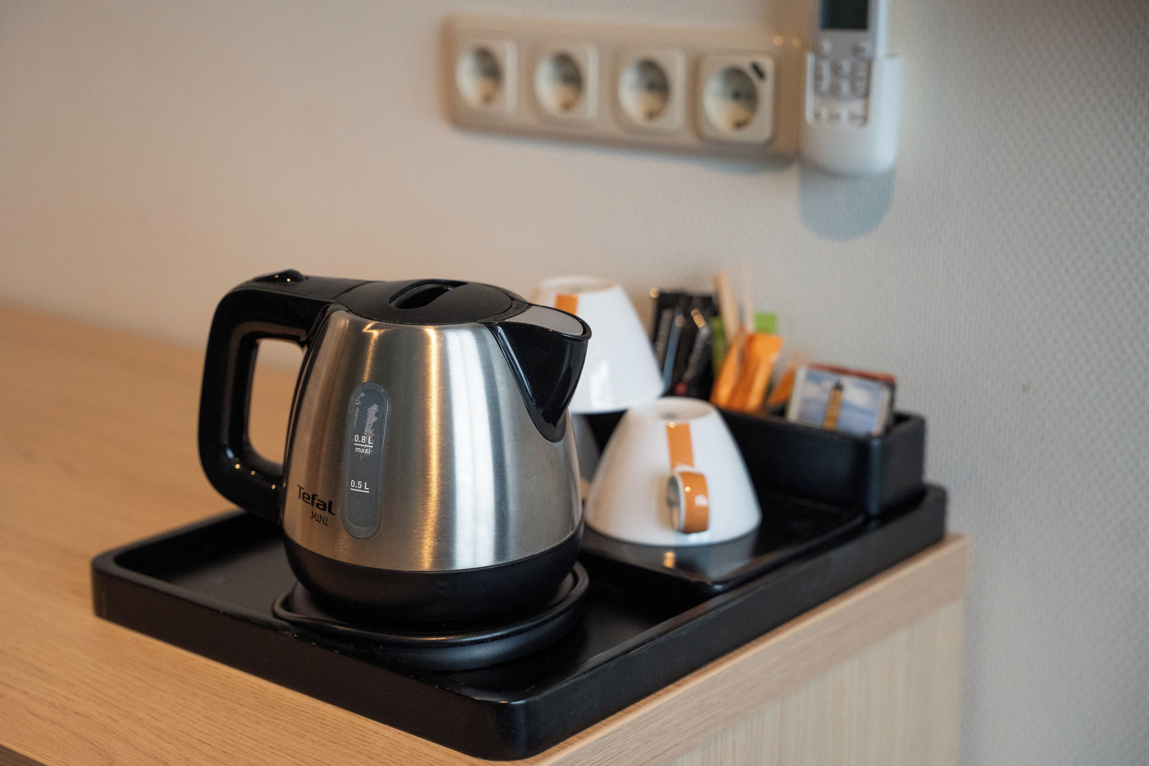 A kitchen area with a kettle, a coffee maker, and a tea kettle on a black tray.