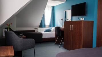 A bedroom with a bed, a desk, a chair, a TV, and a wardrobe.