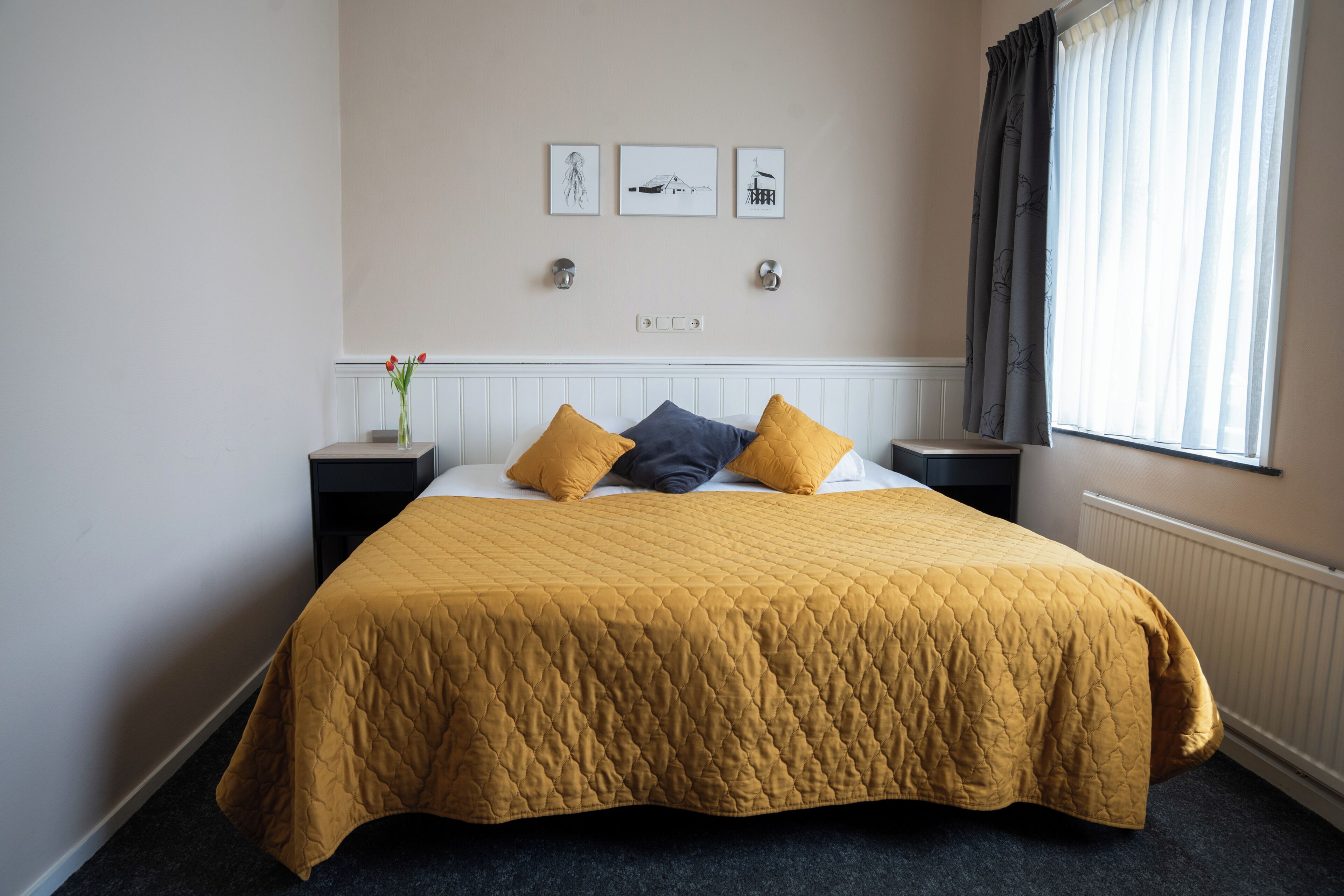 A hotel room with a large bed, a nightstand, a vase with flowers, and artwork on the wall.