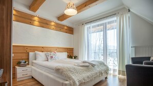 Quarto com teto de madeira, uma cama grande com manta branca fofa, uma mesinha de cabeceira e uma cadeira.
