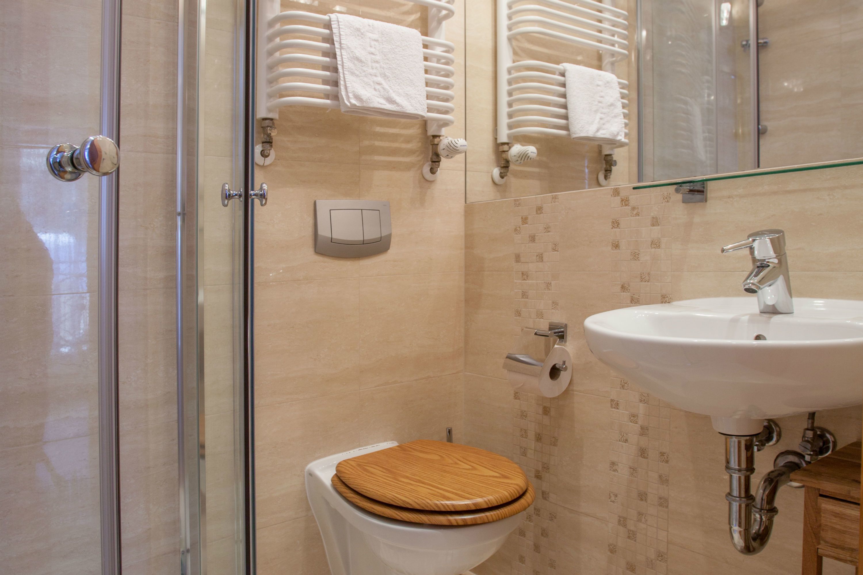 Un baño con cabina de ducha de vidrio, un inodoro blanco con asiento de madera, un lavabo blanco con grifo cromado y un espejo sobre el lavabo.