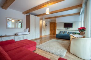 A spacious living area with a red sofa, a white armchair, and a blue sofa. There is a wooden ceiling with exposed beams, a flat-screen TV mounted on the wall, and a large mirror above the sofa. - Willa Ryś (Zakopane)