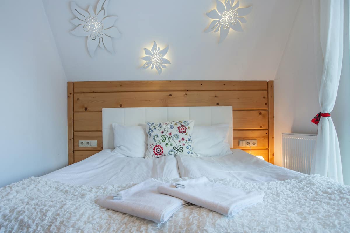 Un lit bien fait, avec du linge de lit blanc et deux serviettes pliées, une tête de lit en bois et des appliques murales décoratives.