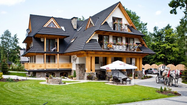 Um edifício grande, com vários andares, uma varanda imponente, área de estar coberta ao ar livre e serviço de carruagem puxada a cavalo.