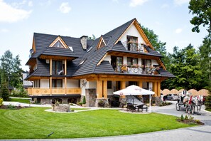 A large, multi-story building with a prominent balcony, a covered outdoor seating area, and a horse-drawn carriage service. - Willa Ryś (Zakopane)