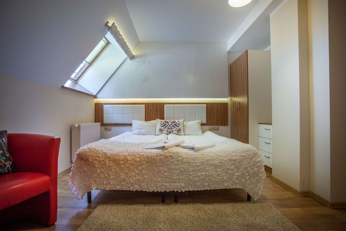 Une chambre avec un grand lit, un fauteuil rouge, un radiateur et une lucarne.
