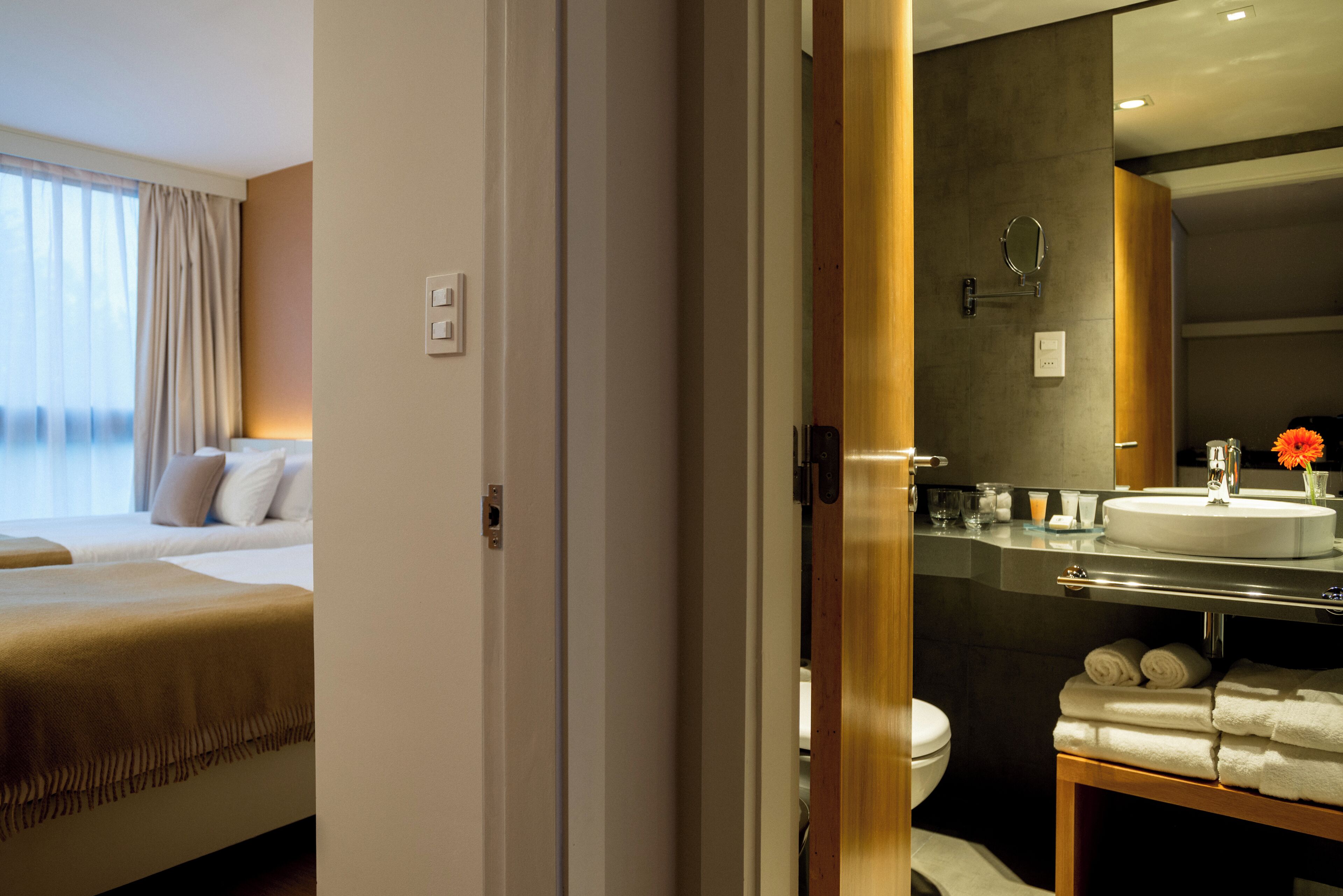 Habitación de hotel con cama, baño con lavamanos y espejo, y vista al mar por la ventana.