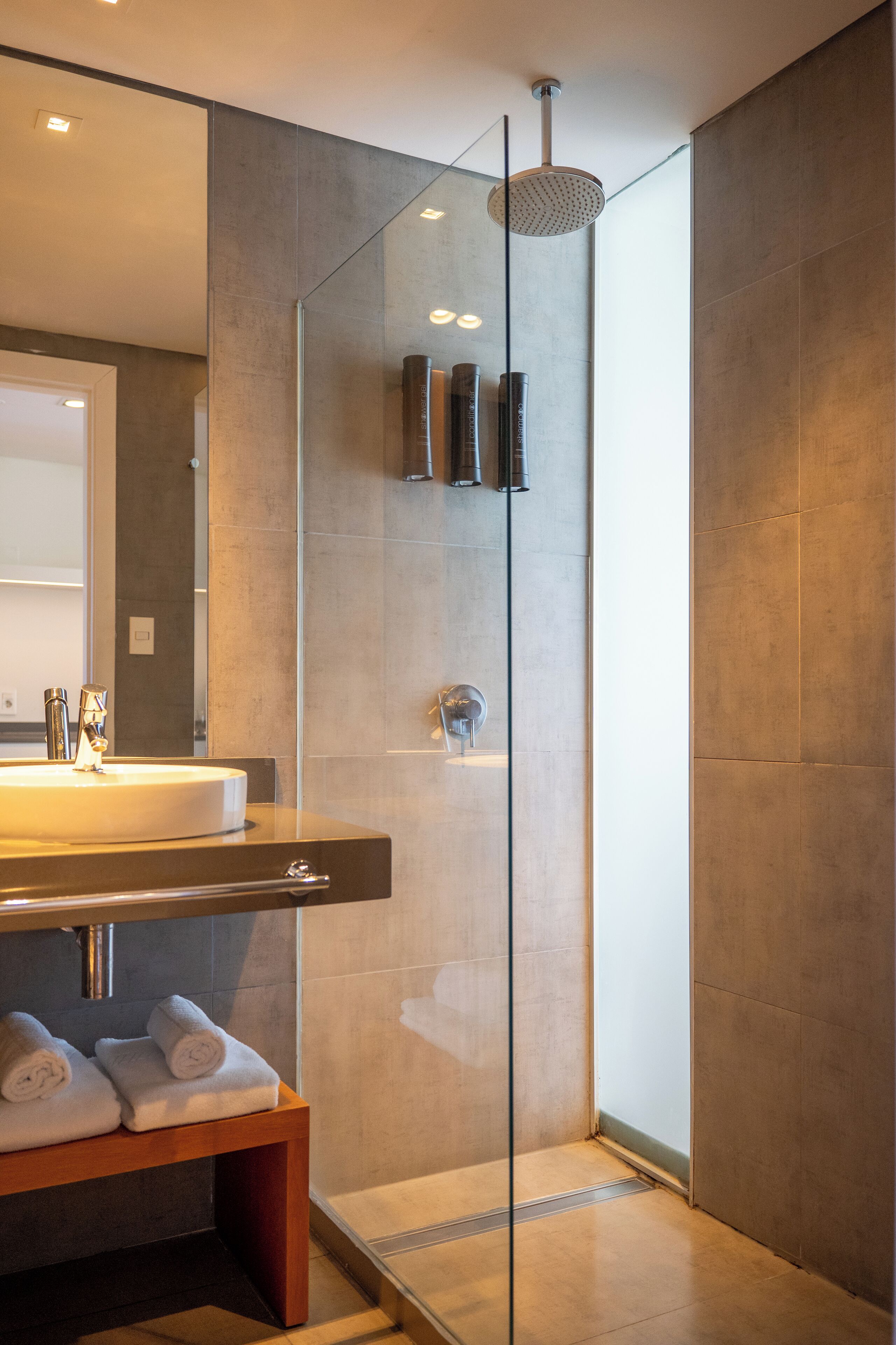 Un baño moderno con ducha de vidrio, tocador con lavabo y banca con toallas.