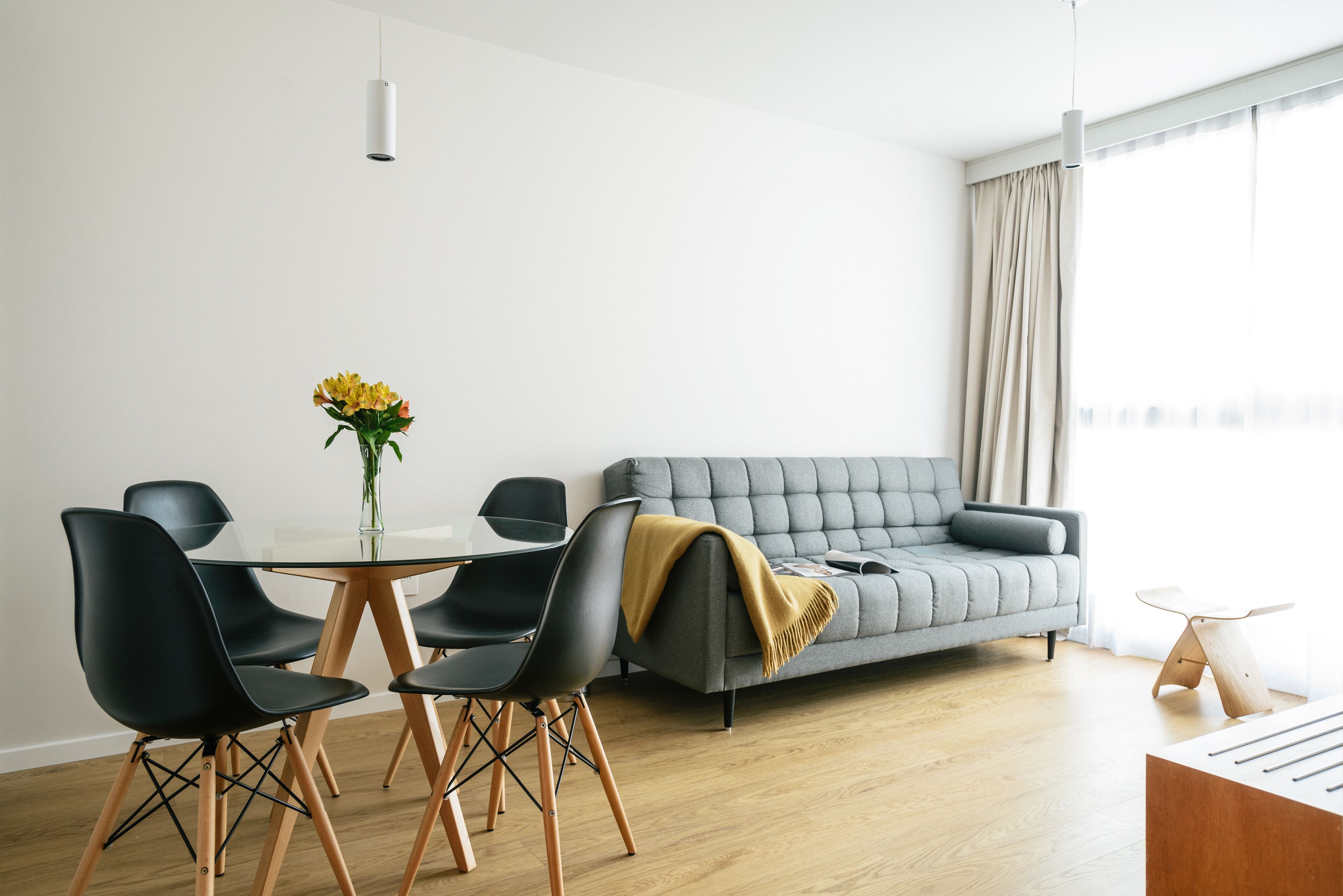 A modern living room with a grey sofa, black chairs, a glass table, and a vase of yellow flowers.