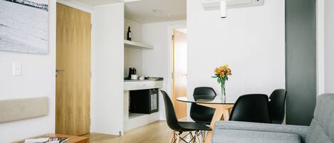 A modern living room with a grey sofa, a wooden bench, and a dining area with a glass table and black chairs.