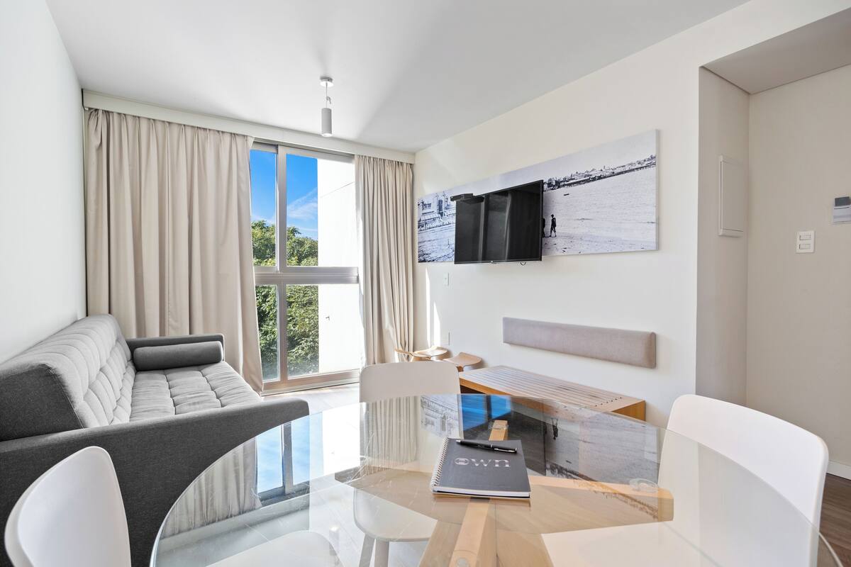 A modern living room with a sofa, a glass dining table, and a mounted TV.