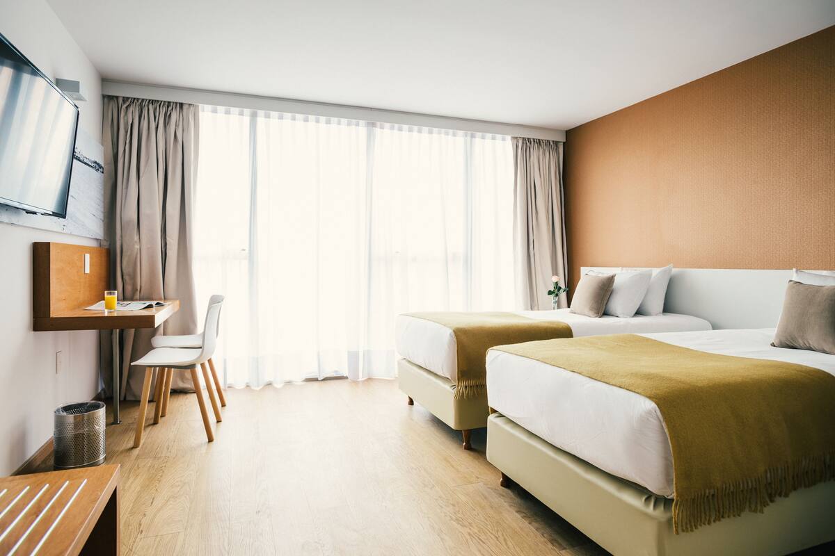 A hotel room with two beds, a desk, a chair, and a TV.