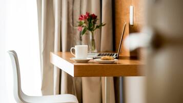 Una mesa de madera con una computadora portátil, una taza blanca y un plato con un pastel. Una silla blanca está a la izquierda.