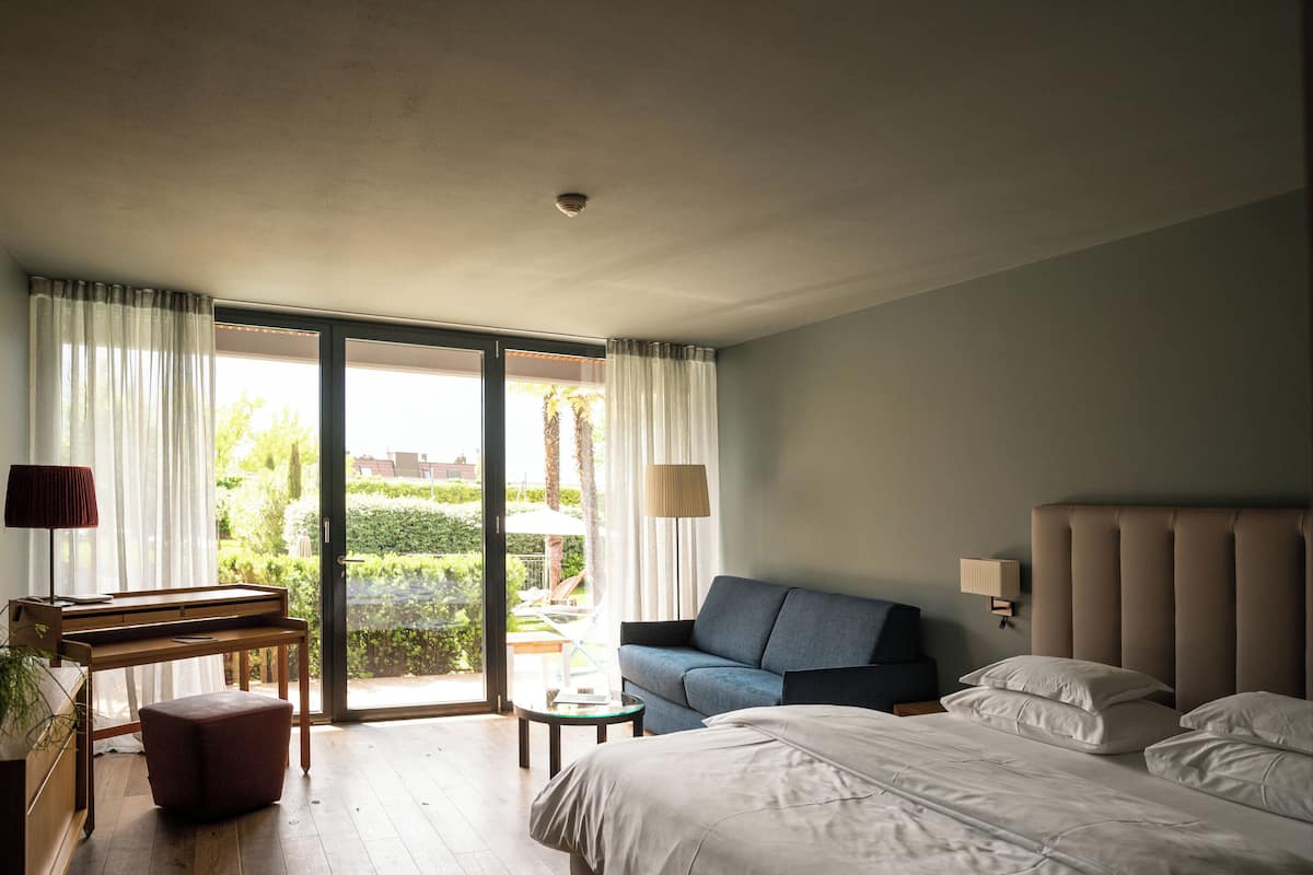 A hotel room with a bed, a sofa, a piano, and a view of the outdoors.