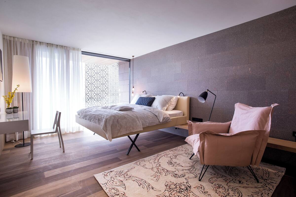 A modern bedroom with a bed, a desk, a chair, and a patterned rug.