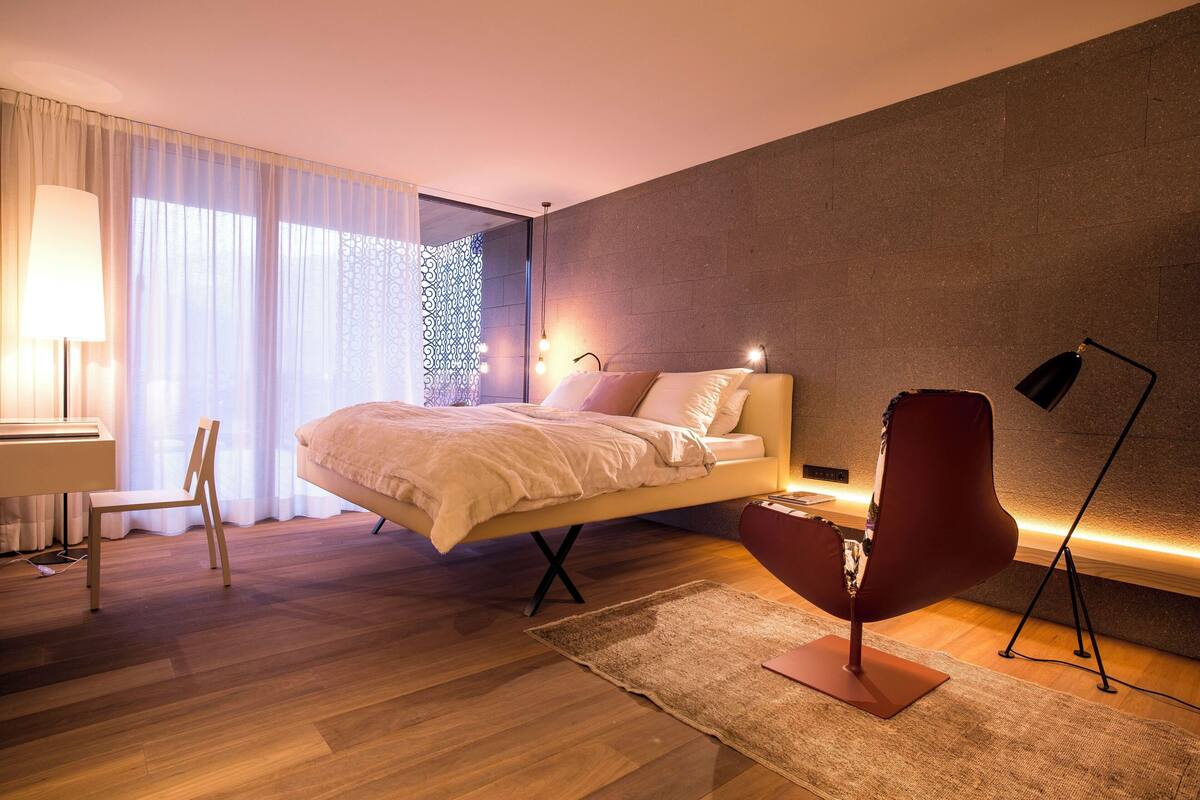 A modern bedroom with a bed, a desk, a chair, and a floor lamp.