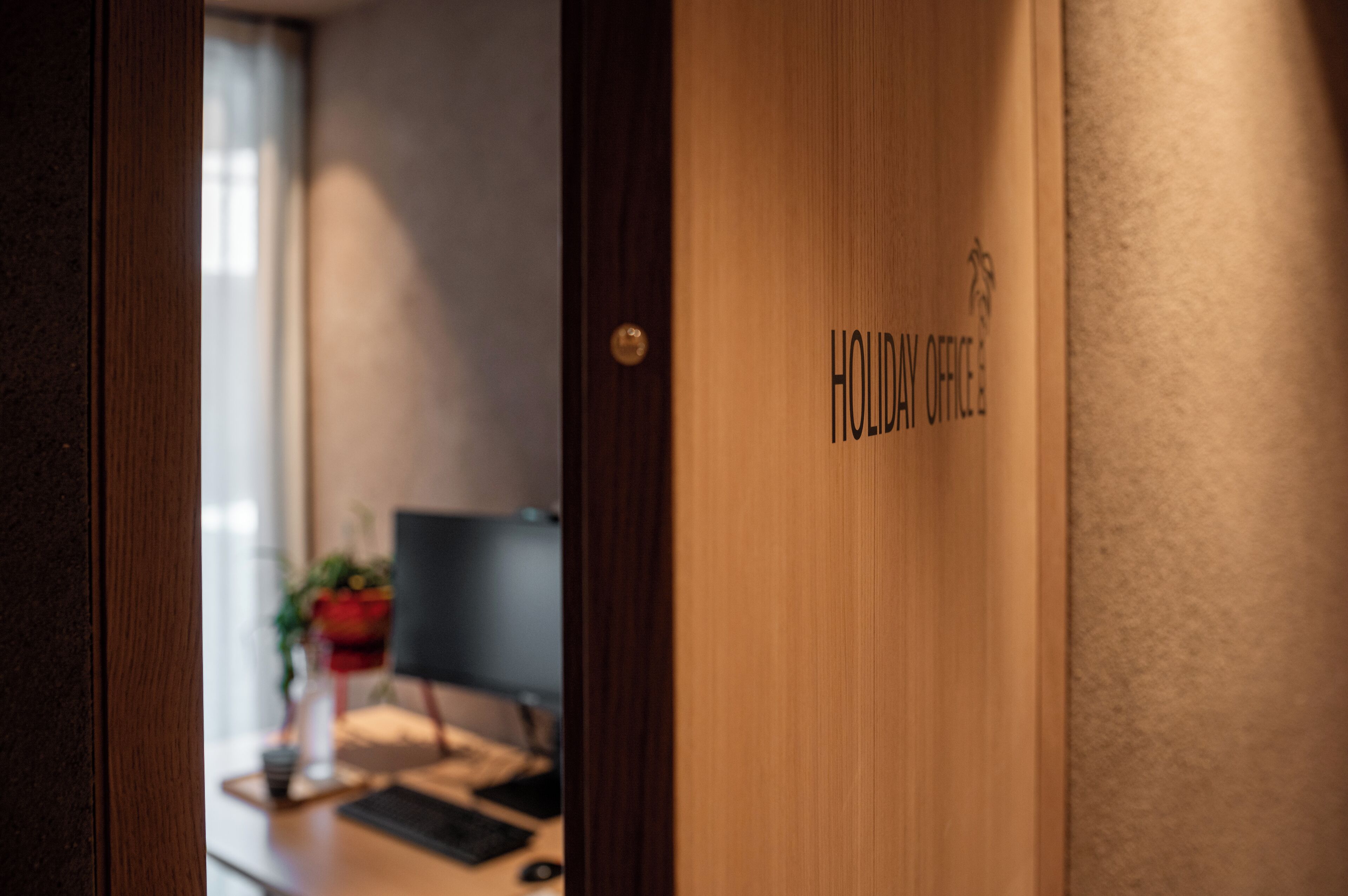Een houten deur met de tekst 'HOLIDAY OFFICE' en een klein logo.
