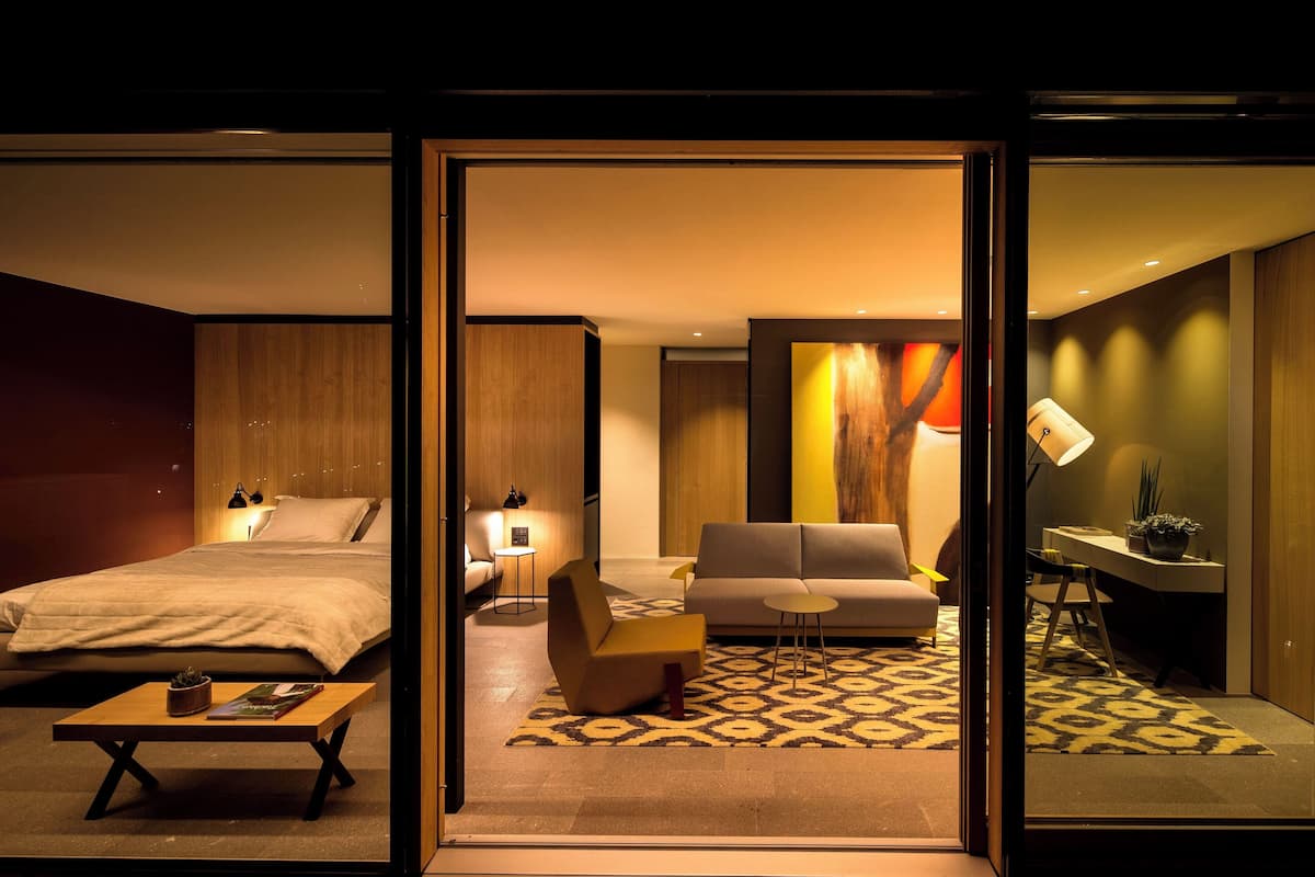 A modern hotel room with a bed, sofa, and desk area.