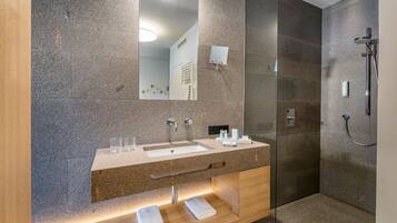A modern bathroom with a granite countertop, two sinks, a glass shower enclosure, and a large mirror.