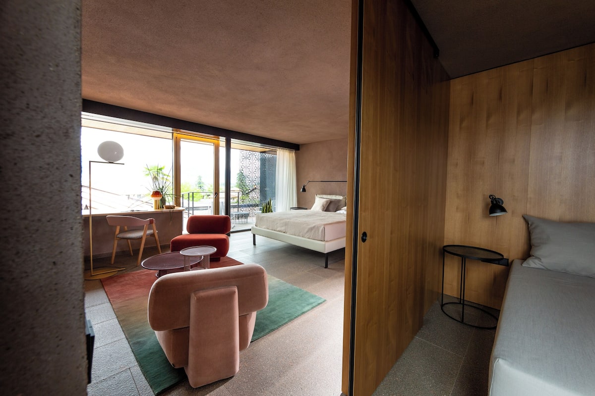 A modern bedroom with a bed, a small desk, a chair, and a sofa.