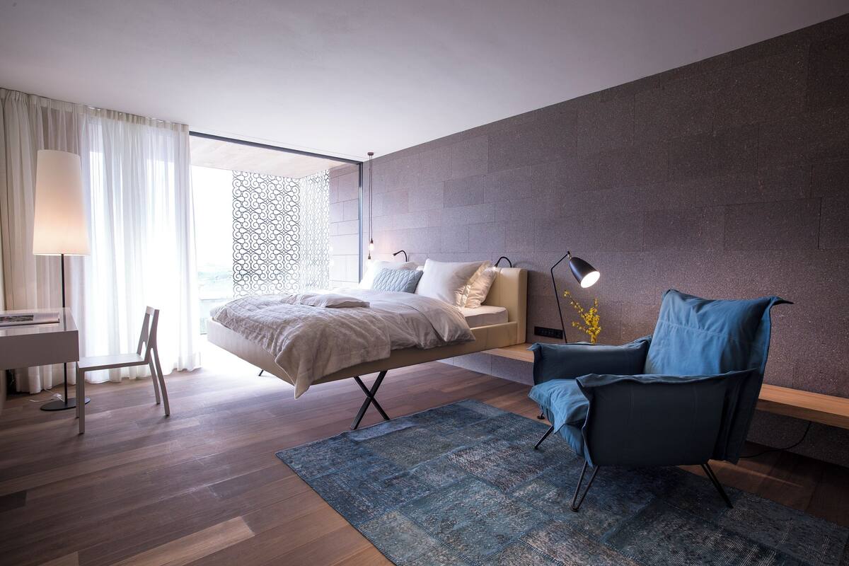 A modern bedroom with a bed, a desk, a chair, and a large window.
