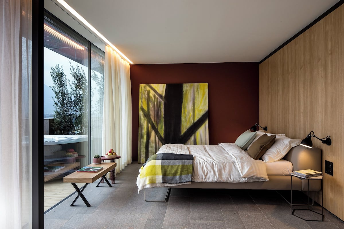 A modern bedroom with a large bed, bedside tables, a window with curtains, and a painting on the wall.