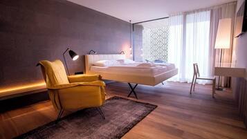 Moderni hotellihuone, jossa on sänky, keltainen nojatuoli, työpöytä ja suuri ikkuna, jossa on verhot.