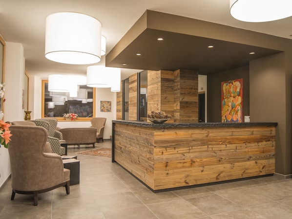 Un espace d’accueil doté d’un comptoir de réception en bois, de fauteuils confortables et de luminaires suspendus.