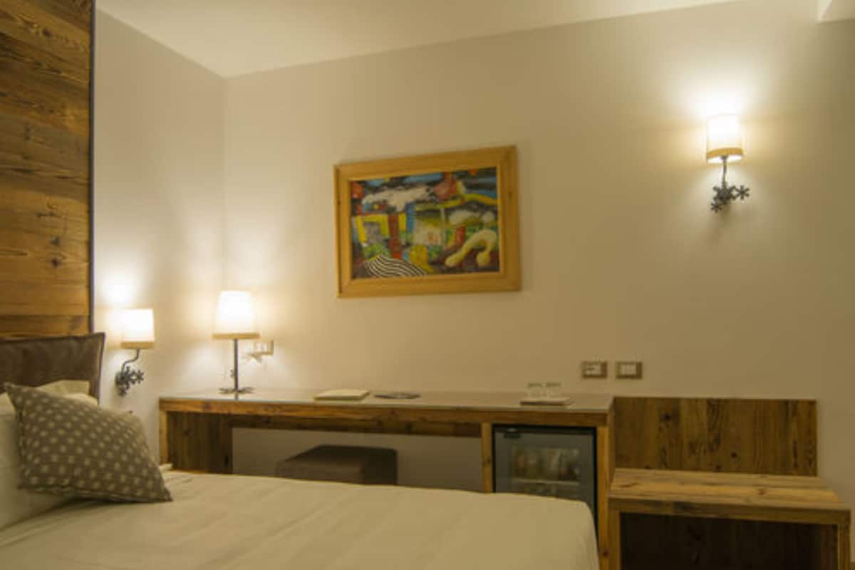 A bedroom with a bed, a desk, a chair, a small table, and a wall-mounted painting.