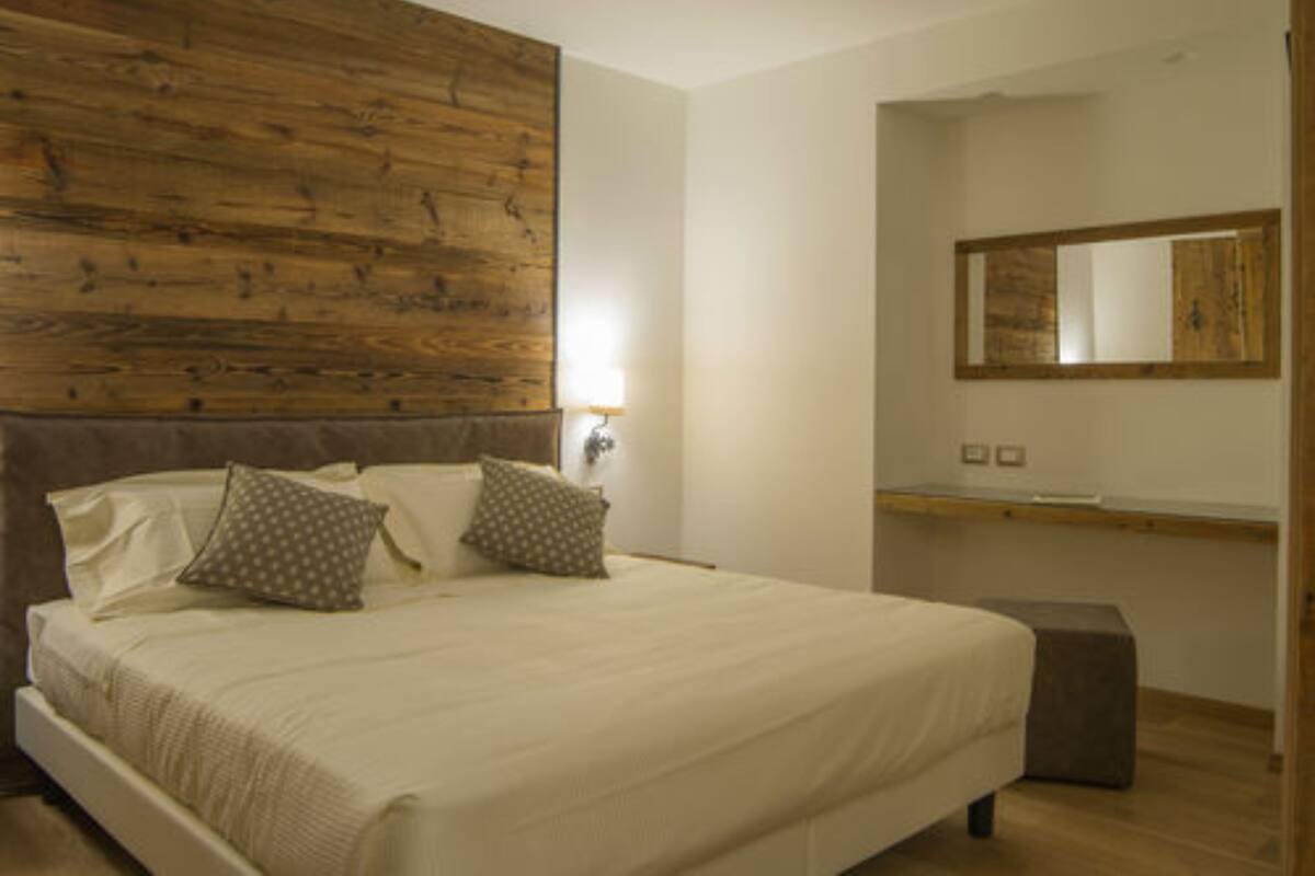 A bedroom with a wooden headboard, a bed with white bedding, two pillows, a nightstand, and a mirror on the wall.