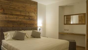 Quarto com cabeceira de madeira, cama com roupa de cama branca, duas almofadas, mesa de cabeceira e espelho na parede.