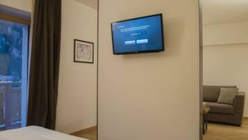A hotel room with a bed, a television mounted on the wall, a framed picture, and a window with curtains.