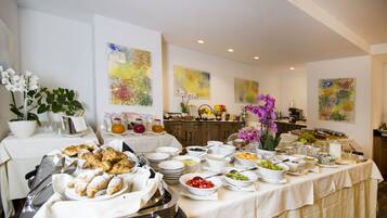 Uma mesa de buffet com diversos alimentos e bebidas, cercada por obras de arte nas paredes.