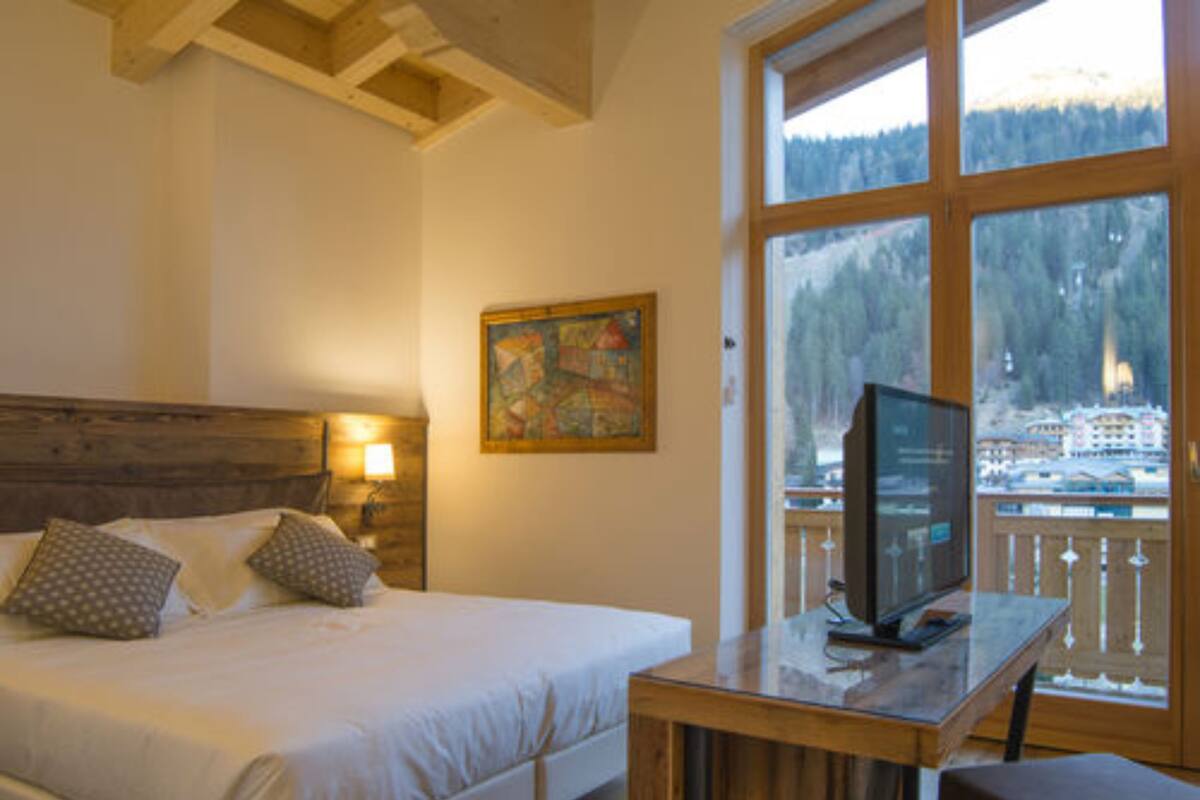 A bedroom with a bed, a wooden headboard, a painting, a TV on a wooden table, and a view of a snowy landscape through large windows.