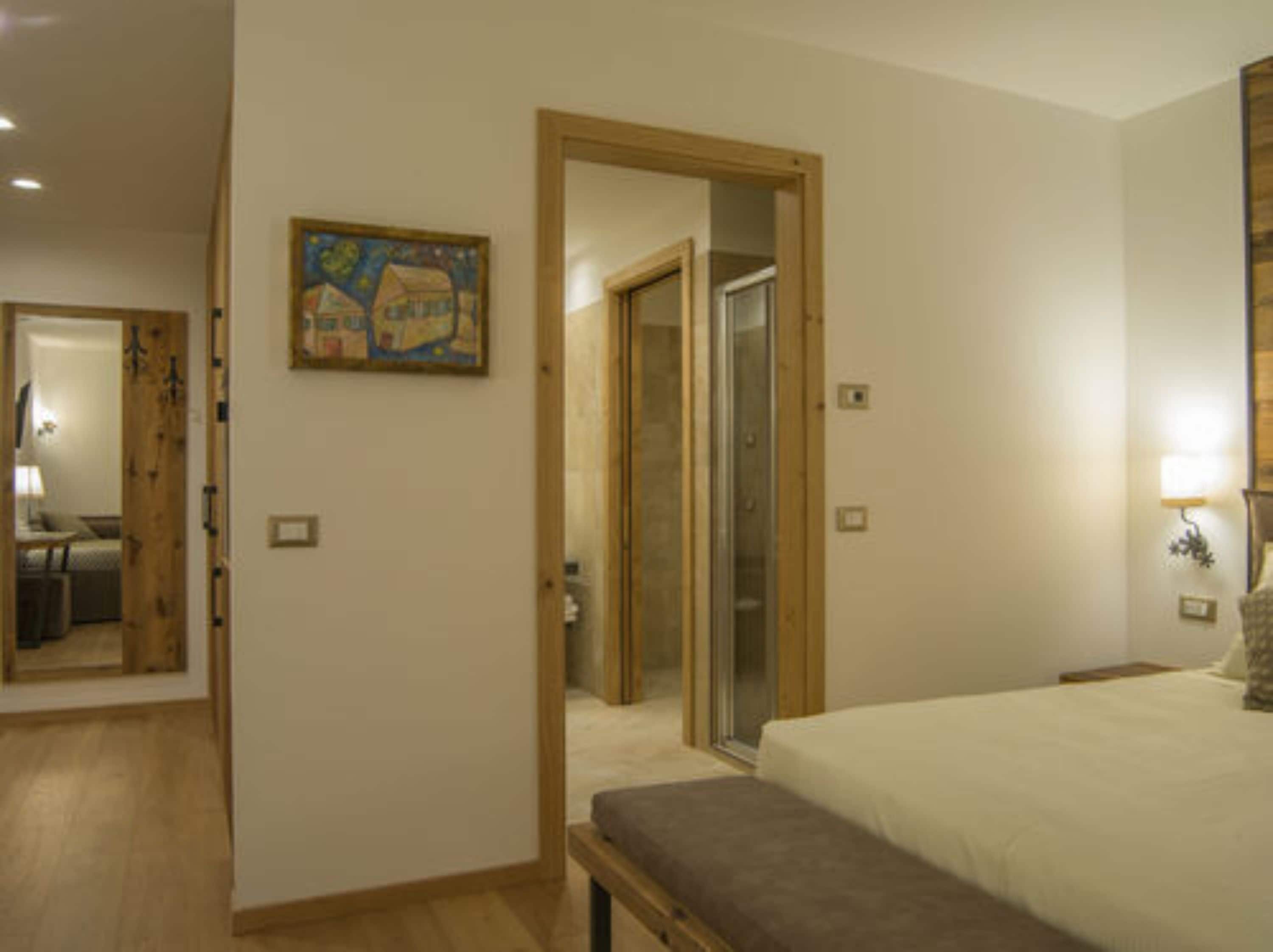 Ein Schlafzimmer mit einem Bett, einer Bank, einem Gemälde und einer Tür zu einem Badezimmer.