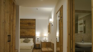Un dormitorio con cabecera de madera, cama, mesitas de noche con lámparas, y un baño con lavabo y espejo.