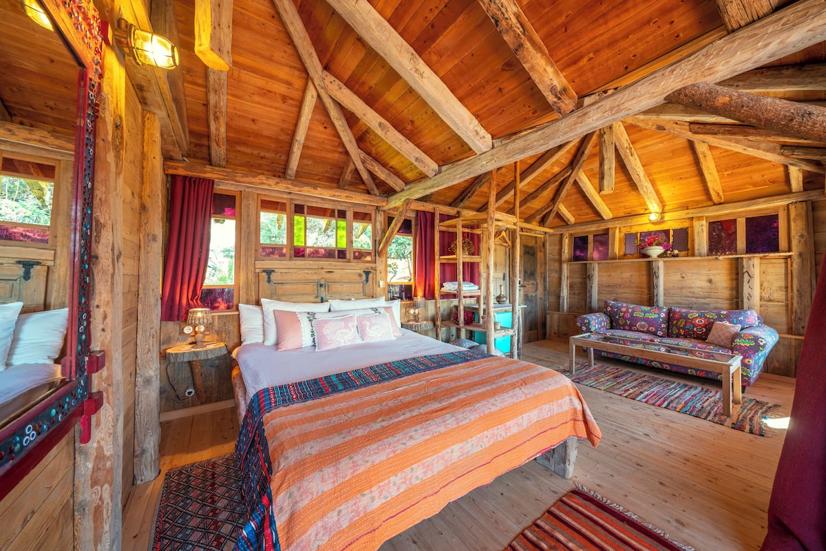 A log cabin room with a large bed, a sofa, and a wooden ceiling.